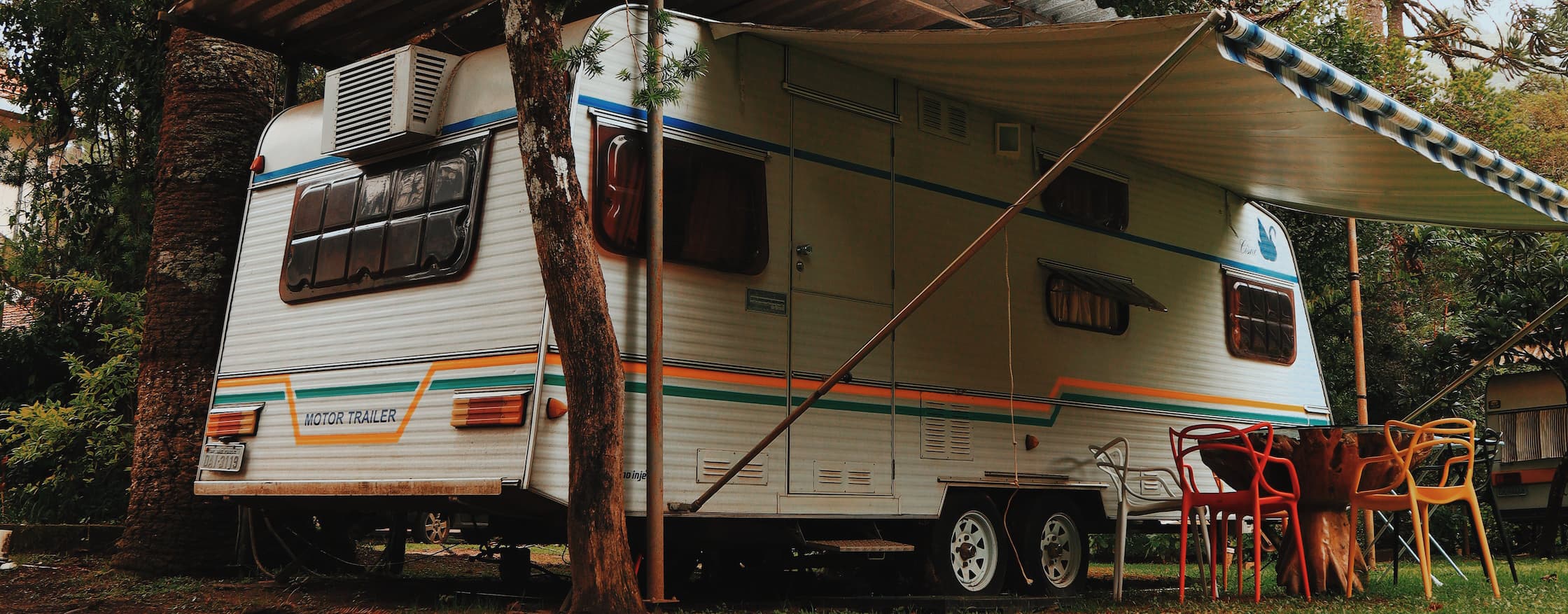 A picture of an RV trailer camping under several pine trees.
